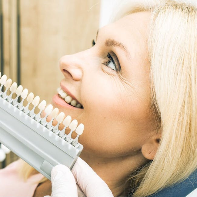 Blonde woman in dental clinic selecting enamel shade for smile improvement.