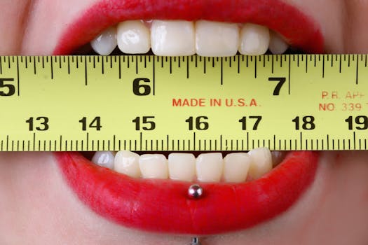 Close-up of red-lipsticked mouth holding a yellow tape measure horizontally, demonstrating measurement concept.
